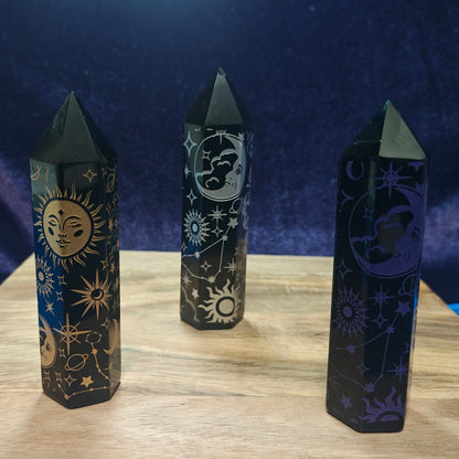 Three black crystal sticks with celestial designs on a wooden surface and blue fabric background