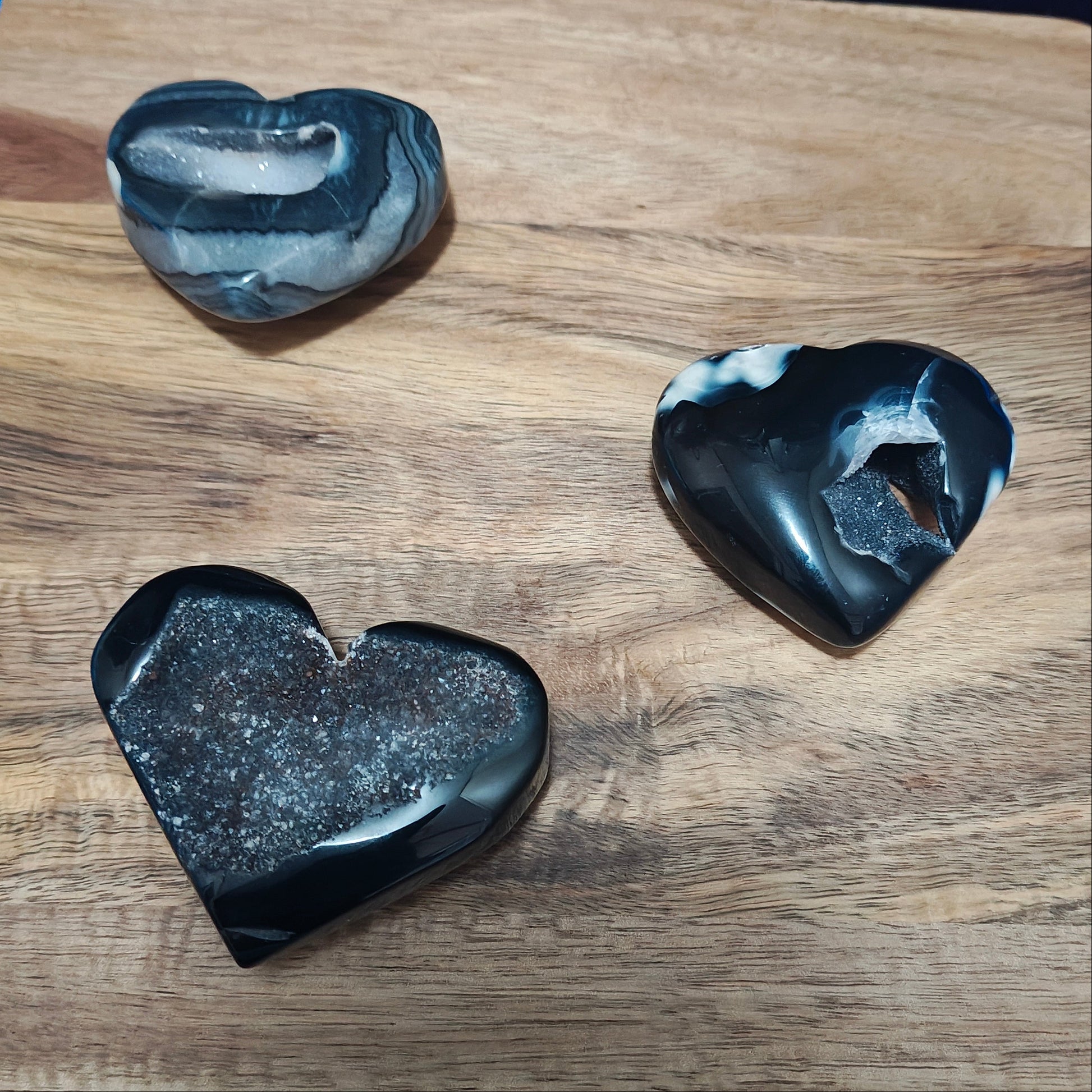Three heart-shaped black stones on a wooden board with a blue fabric background