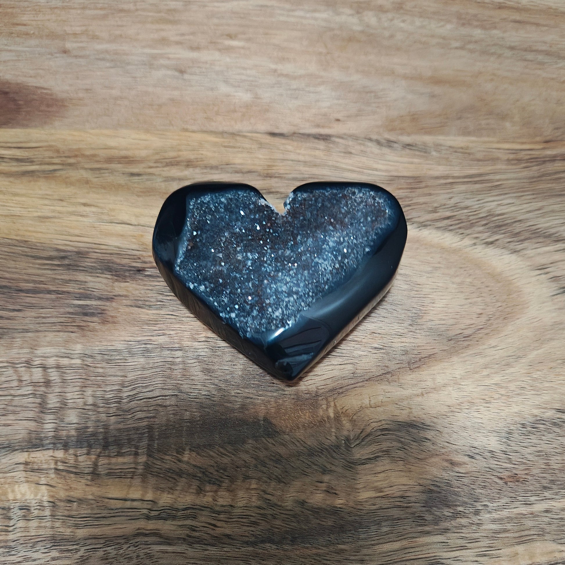 Heart-shaped black stone on a wooden surface with a blue fabric background