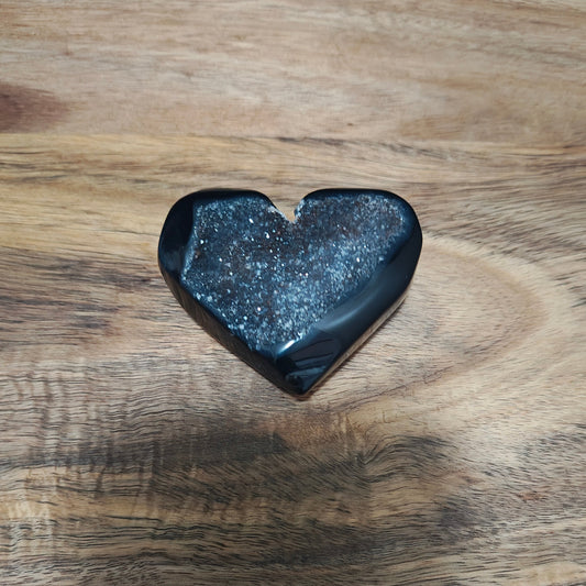 Heart-shaped black stone on a wooden surface with a blue fabric background
