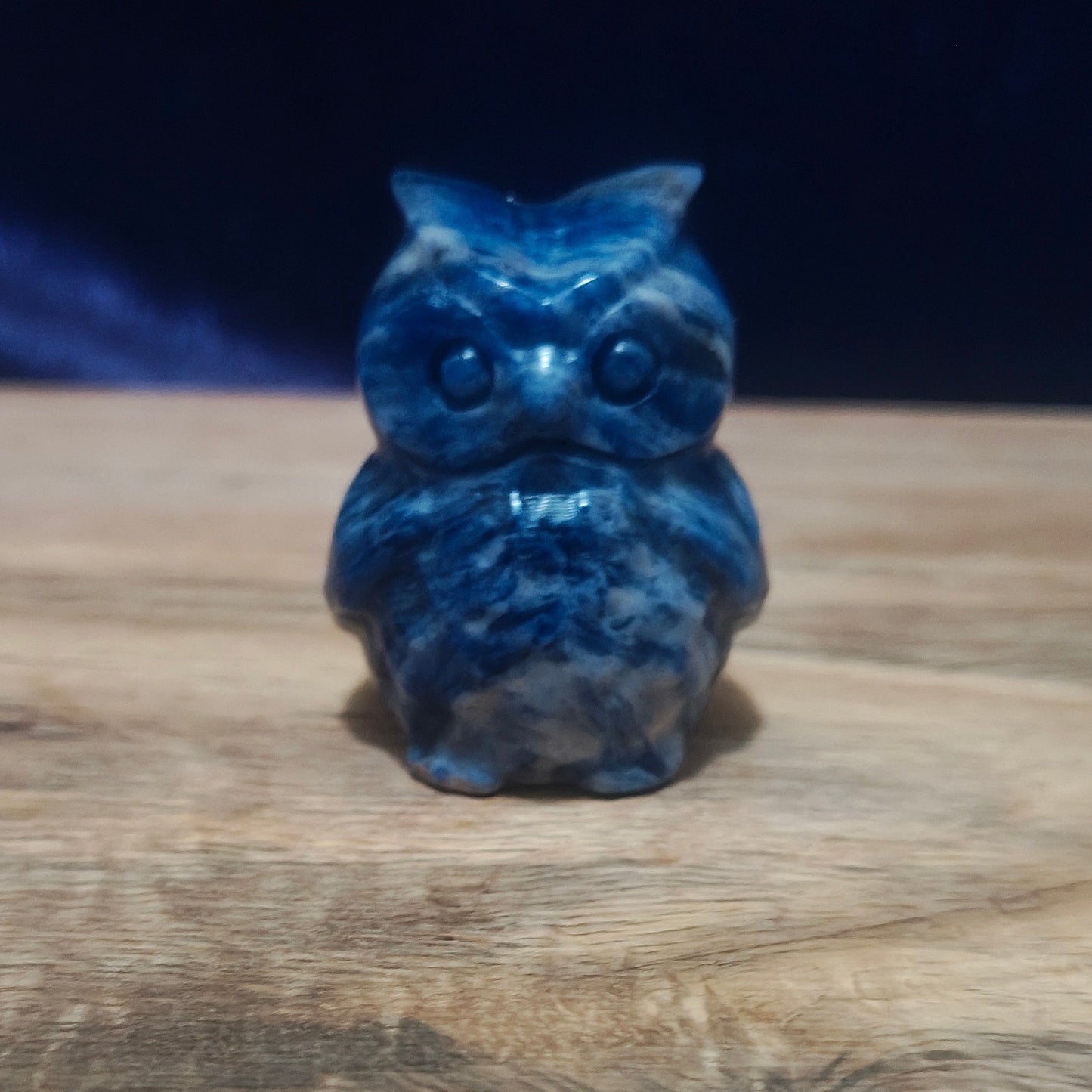 Blue owl figurine on a wooden surface with a dark background