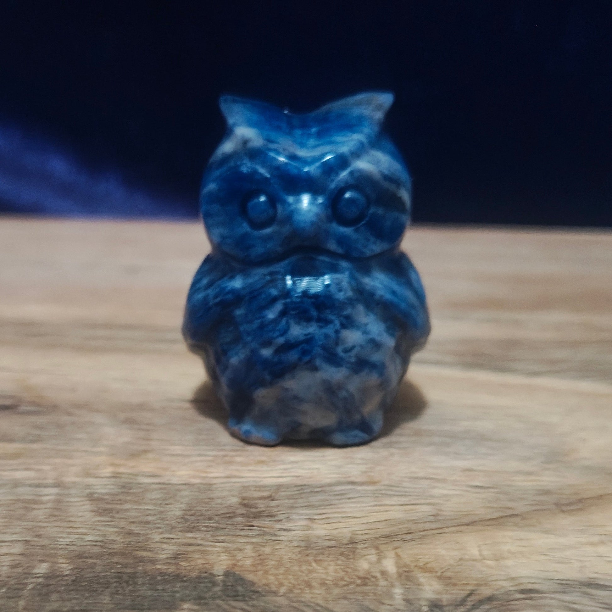 Blue owl figurine on a wooden surface with a dark background